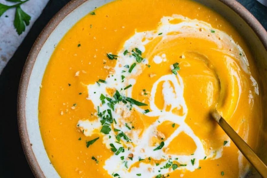 A bowl of creamy carrot soup topped with herbs.